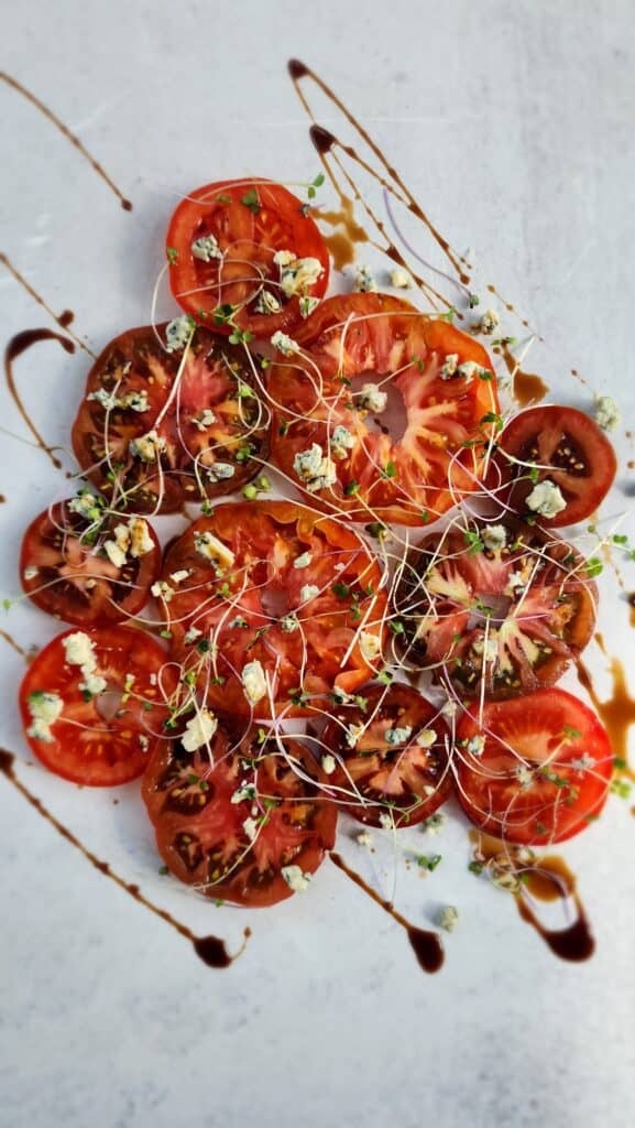 Heirloom Tomatoes cut in slices with blue cheese crumbled on top with sprouts and a drizzle of balsamic glaze