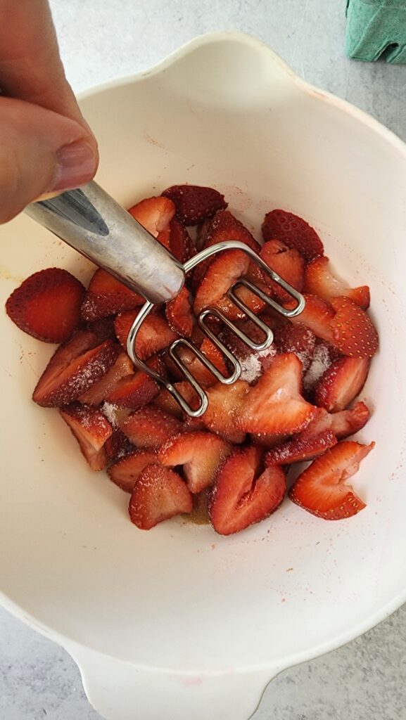 mashing sliced strawberries in a bowl