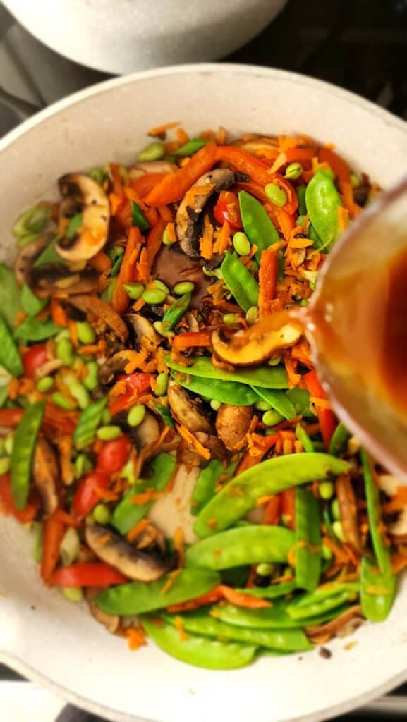 adding the stir-fry sauce to easy veggie stir-fry skillet