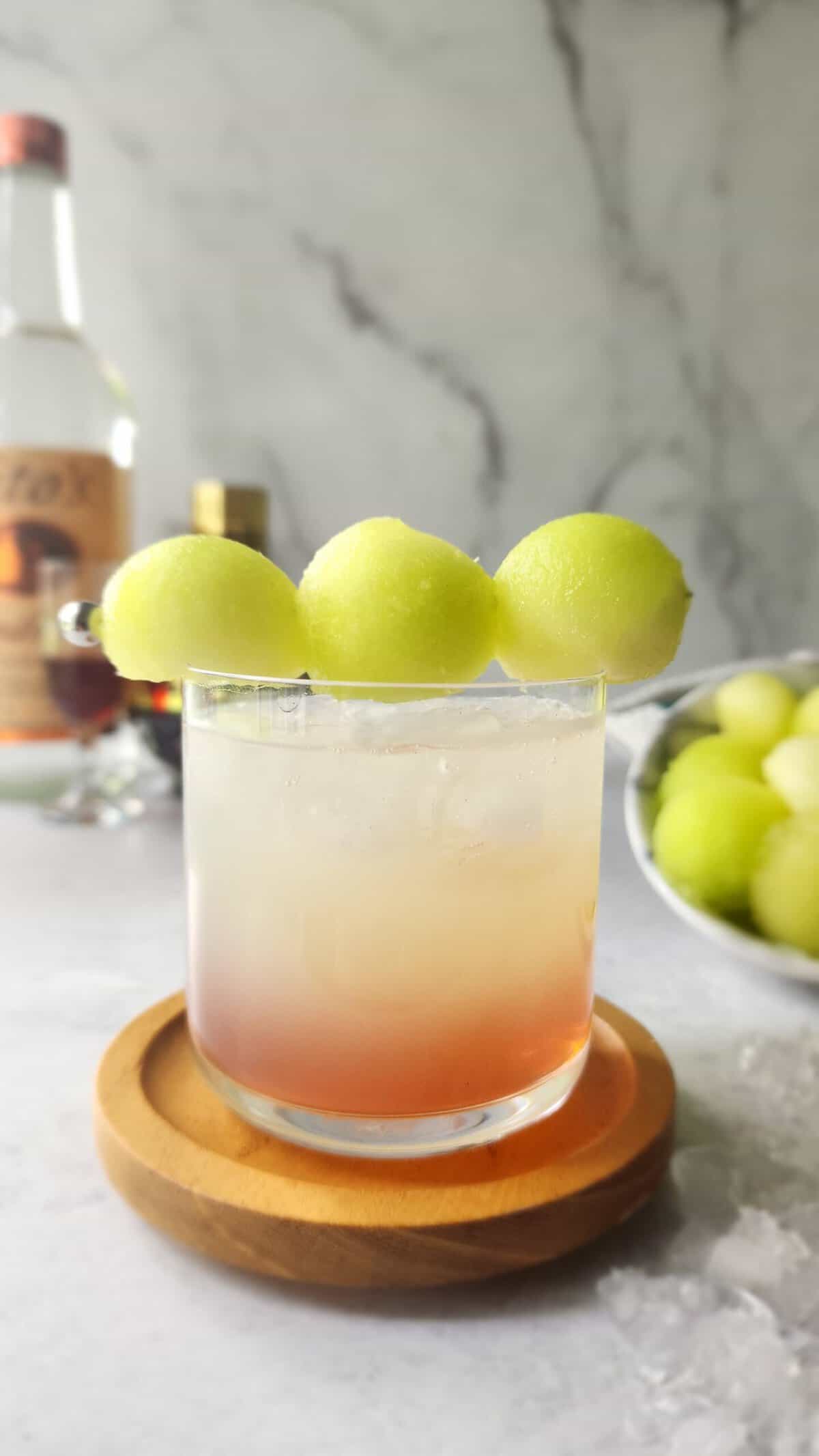 Glass of the honey deuce cocktail with a skewer of honeydew melon balls simulating 3 tennis balls