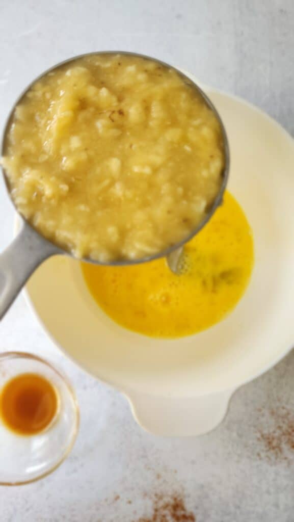 Mashed banana being added to a bowl of whisked eggs for baby's 1st smash cake