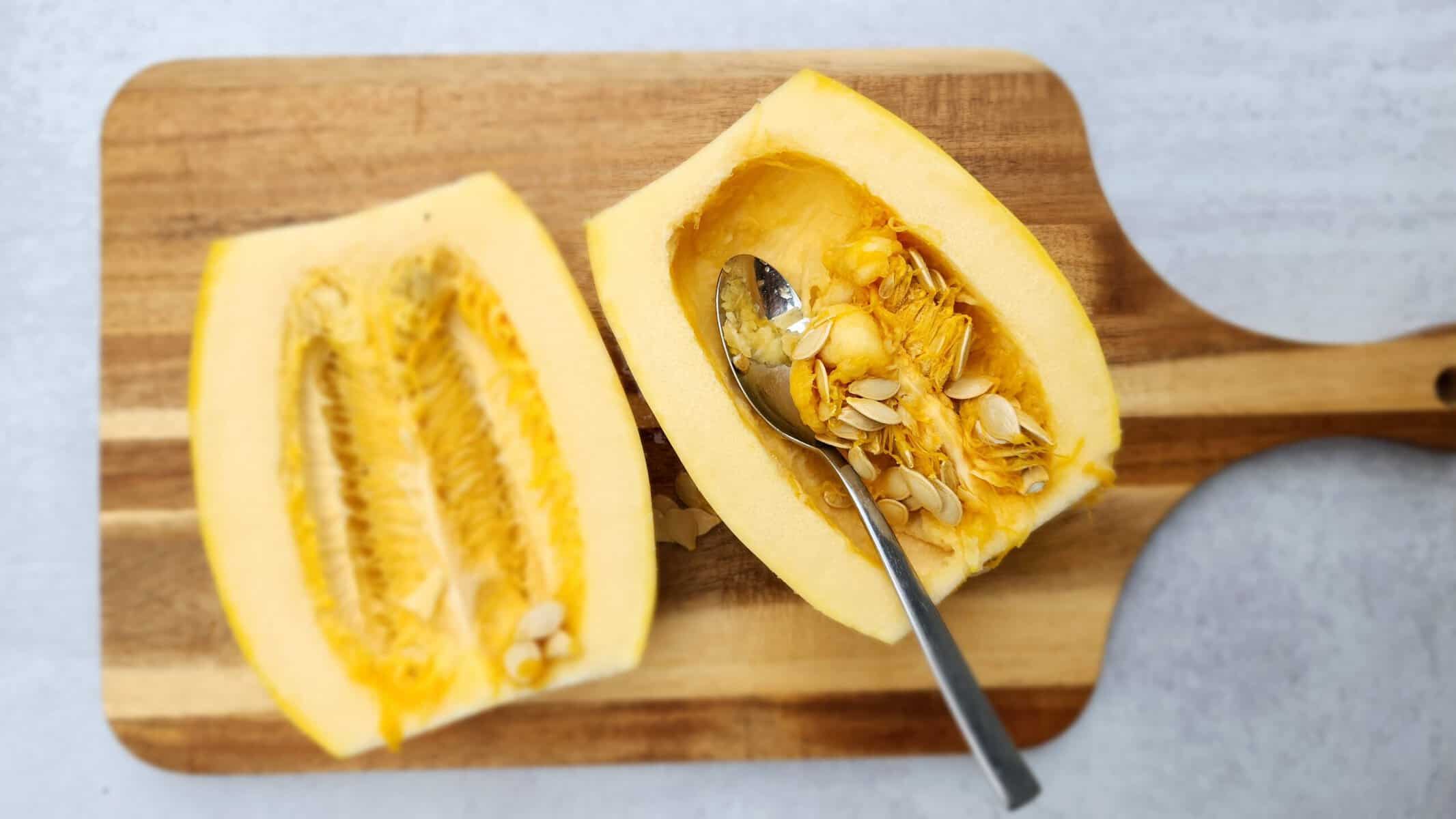 Spaghetti Squash cut in half on a wood cutting board with a spoon scooping out the seeds