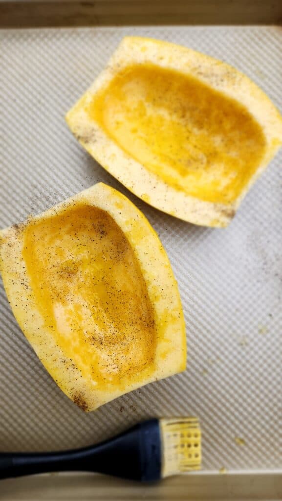 spaghetti squash cut in half after olive oil is drizzled on with a brush