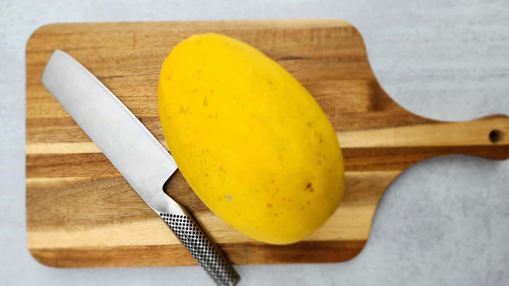 Spaghetti squash and a sharp chef's knife on a wood cutting board ready to cut